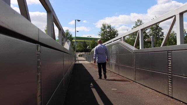 Caucasian male walking across a bridge at a train station platform on a beautiful sunny day located in the village of Castleford in Wakefield West Yorkshire UK, showing the British train station