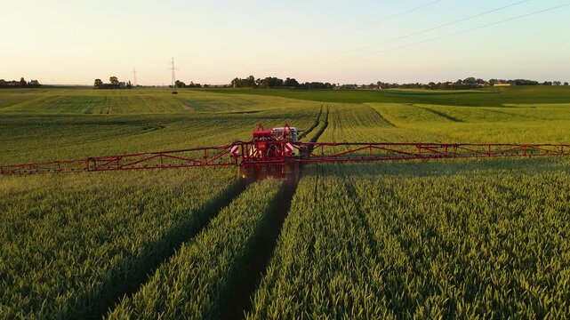 Farmer on tractor working on field with sprayer, spraying herbicides and pesticides at sunset aerial view. Agronomic ecologically plants growing on fertility soil