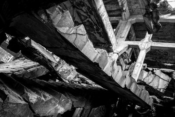 A monochrome photograph captures the haunting beauty of an abandoned building’s interior with a crumbling staircase and fractured concrete.