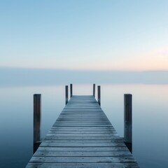 Fototapeta premium A wooden dock extends into a tranquil lake shrouded in morning mist. The serene scene evokes feelings of peace and solitude.