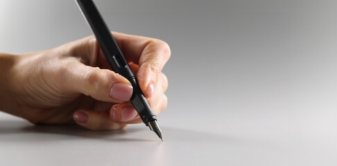 Female fingers hold a black fountain pen on a gray background, close-up. Correspondence concept, copywriting