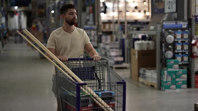 Front view of young happy man pushing shopping cart in hardware store.