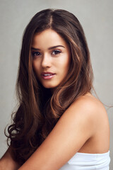 Naklejka premium Woman, portrait and beauty with haircare for makeup or cosmetic treatment on a gray studio background. Face of young female person, brunette or attractive model for hair, glow or shine in salon care
