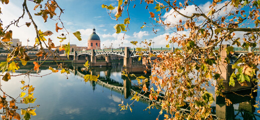 La Grave Hospital Reflected in the Garonne River at Sunrise, Framed by Lush Foliage in the Foreground and Bathed in Golden Light Under a Clear Blue Sky, Toulouse