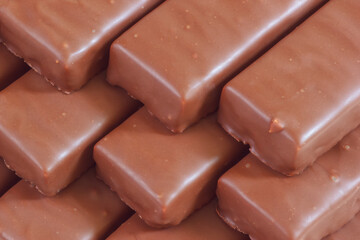 The rows of chocolate bars. The sweet dessert confectionery with brown glaze. The yummy food with a lot of calories. Closeup view.