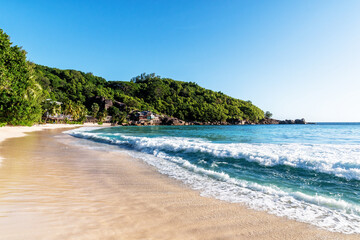 Panoramic view of tropical beach with white sand, clear turquoise water. The waves are crashing on the shore, creating a sense of tranquility