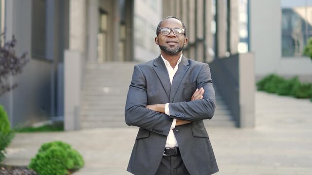 Confident african american man in formal business suit standing ams crossed in urban office setting. Professional portrait depicting success, leadership. businessman looks at camera outdoors