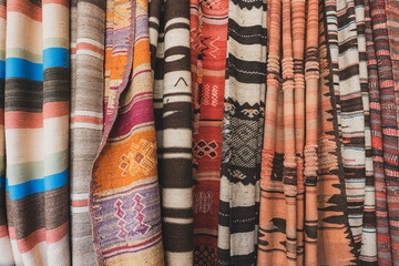 Closeup of Moroccan Textiles, wool rugs and blankets display, colorful earthy woven traditional fabric with Intricate geometric Patterns, horizontal background texture, Atlas Mountains, Morocco