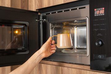 Person placing mug with drink in microwave