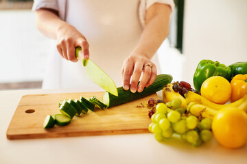 Hands, person and cucumber for cooking in kitchen with knife, cutting or meal prep for wellness in home. Chef, fruits and food with organic product for benefits, nutrition or diet for health in house