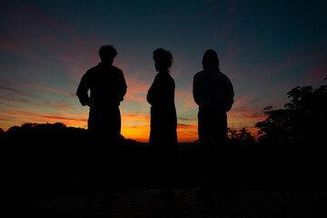 Three people in darkness, men, and women, looking into the distance under  sunset