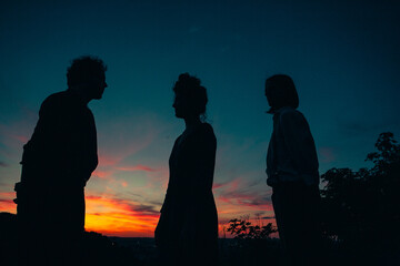 Dark evening and meeting of three people, two men and one women, under sunset	