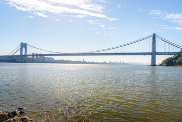 View of majestic George Washingtong bridge spanning Hudson river on a clear autumn day. Manhattan downtown is visible in distance.