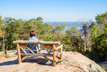 Woman tourist looking at a magnificent view while sitting alone on a wooden bench on the top of a mountain on a sunny autumn day