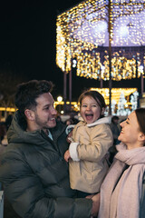 Obraz premium Joyful Family Walk in Alcala de Henares Amidst Christmas Lights. A candid image of a young family enjoying a night Christmas walk in Alcala de Henares.