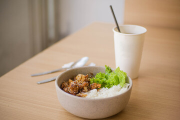 Ricebowl Beef Barbeque in a white bowl on a natural wood color table with ice tea on white paper cup