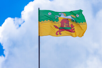 A waving flag with the coat of arms of Novokuznetsk against a cloudy sky, Russia