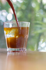 Pouring coffee into a glass of iced water on the table with blurred background	