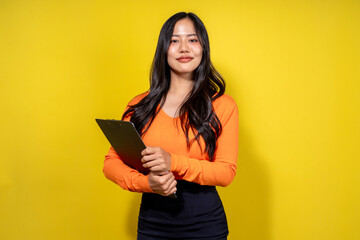 A woman in an orange shirt and black skirt is holding a clipboard