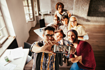 Diverse young professionals taking group selfie in office