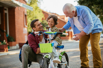 Little boy learning to ride a bike with grandfather and father outside