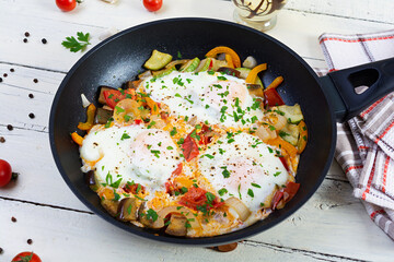 Shakshuka in a frying pan.  Fried eggs with tomato, pepper, zucchini and herbs
