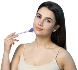 Close-up of a young girl in a light top on a white background making a facial make-up. A pretty woman holds a cosmetic brush near her face and smiles.