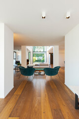 Modern living room with two turquoise armchairs, a coffee table and a sofa with cushions. Large windows overlooking the garden