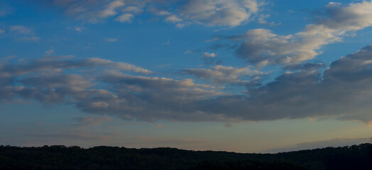 Fototapeta premium Clouds in the evening sky against the backdrop of dark silhouettes of hills.