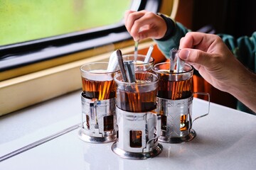 The boy and the man brew black tea in glasses in the cup holders on the table on the train.