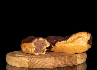 Two eclairs with cream on a wooden tray, macro, isolated on black background.