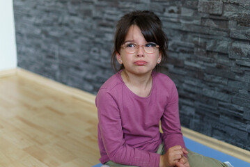 Little offended girl with glasses cries sitting on the floor. Concept of difficult child life