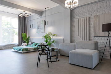 stylish discreet interior of the sleeping area in a modern studio in white-gray colors with green plants. daylight and no people inside