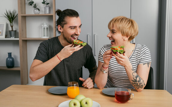 Happy couple enjoying a healthy breakfast with avocado toast and drinks. Smiling and sharing a moment together in a cozy home kitchen.