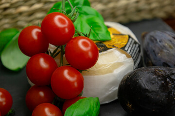 A head of cheese with a juicy branch of cherry tomatoes, green aromatic basil and purple figs on a gray background. Copy space the text. Banner.