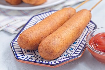 Two corn dogs on white blue plate, served with ketchup, horizontal