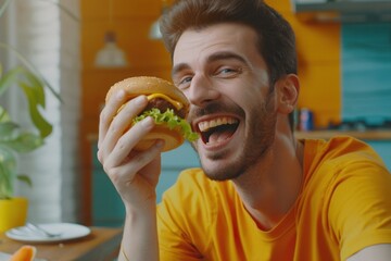 Man enjoying a burger in a yellow shirt, at home