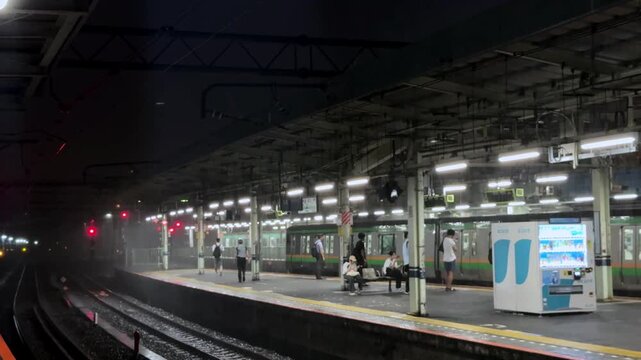 Commuters wait on a platform at Tokyo's Shinagawa Station at night with lights illuminating the scene