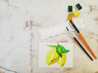 Watercolor lemon drawing, brushes and paints on clear table. Free space for text