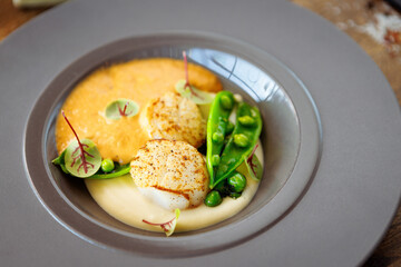 Scallops with shrimp foam, cauliflower cream and green peas on a plate. Delicious healthy seafood closeup served for lunch on a table in modern gourmet cuisine restaurant