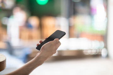 A black cell mobile phone in the hand of a young man in his twenties at a cafe with out of focus street scene in th background