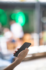 A black cell mobile phone in the hand of a young man in his twenties at a cafe with out of focus street scene in th background