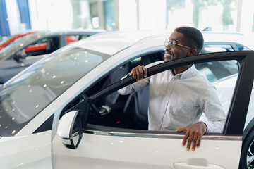 Handsome african american man is touch and test his new car and smiling. Business sales automobile in dealership