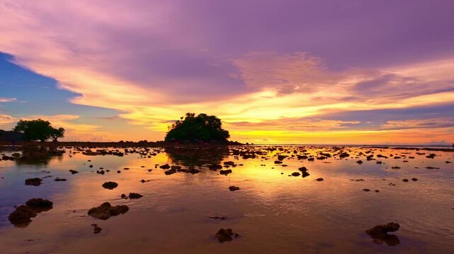 A tranquil seascape during dawn at low tide under a serene sky transitioning from night to day. The sun slowly sets behind the island. The gradien sky changes color bright and colorful