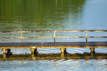 Drewniany pomost nad jeziorem odbicia refleksy na wodzie. © Monika