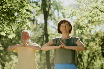 Low angle shot of senior friends with closed eyes staying in open hands vs closed fist position during martial art practice