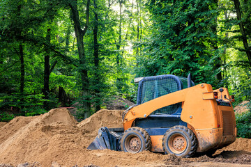 A skid steer loader shovels soil in a park area.