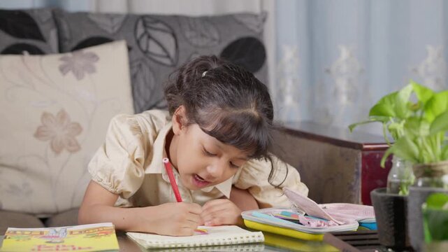Cute South Asian little girl coloring a picture book with colored pencils at home, close up portrait of focused Bangladeshi or Indian female child drawing during creative playtime