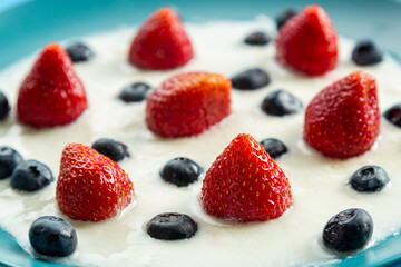 Berries strawberries and blueberries in a plate with thick whipped cream on a blue background