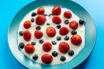 Fresh juicy berries strawberries and blueberries in a blue plate with whipped cream on a blue background